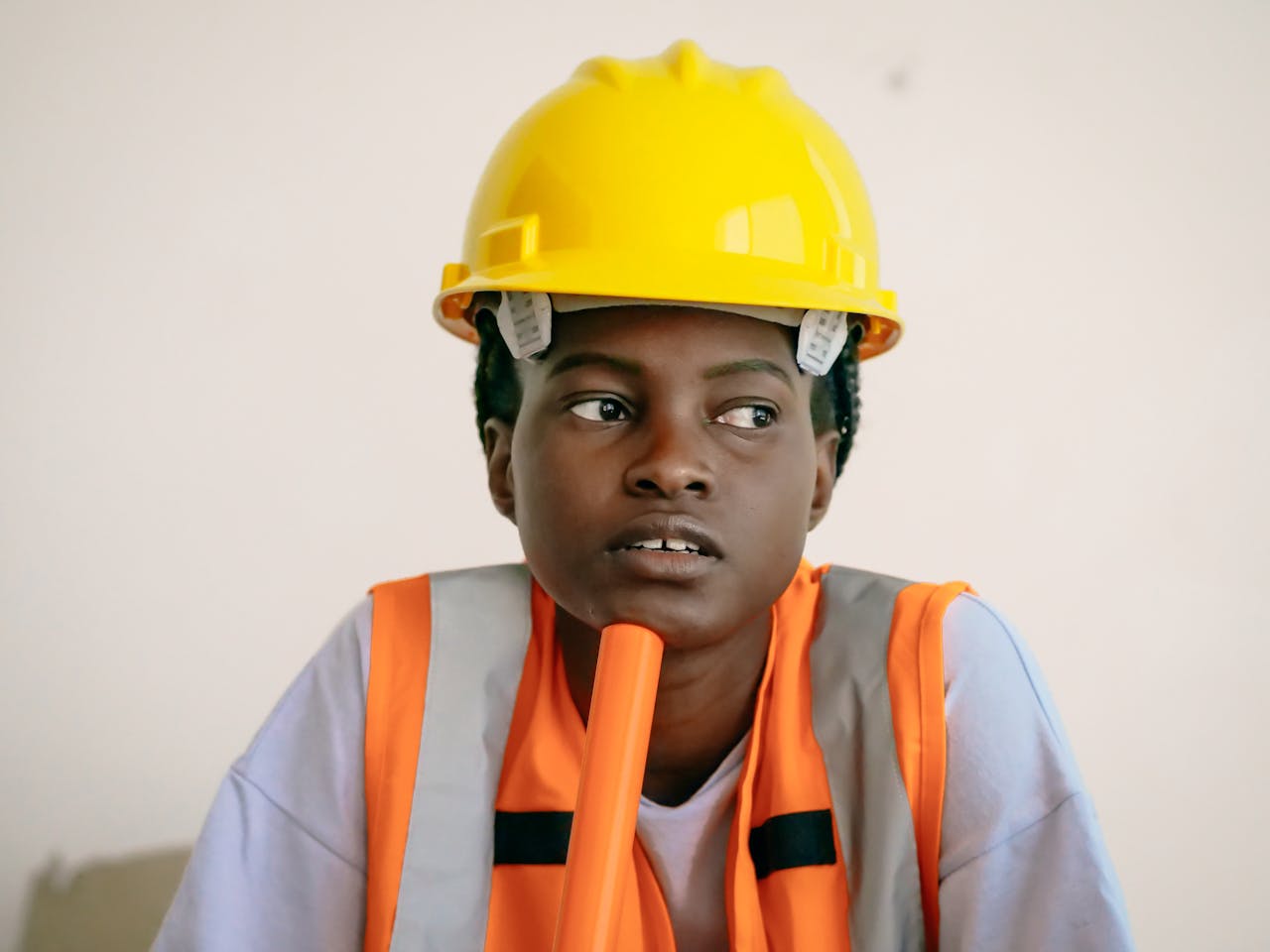 African American woman in safety gear, deep in thought, wearing a hardhat and vest.