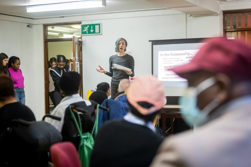 A diverse group attending a community meeting with a presenter speaking in front of a screen.